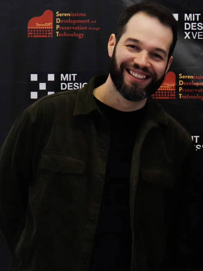 Riccardo Sponchiado smiling, in a dark jacket, in front of the MIT DesignX Venice panel.
